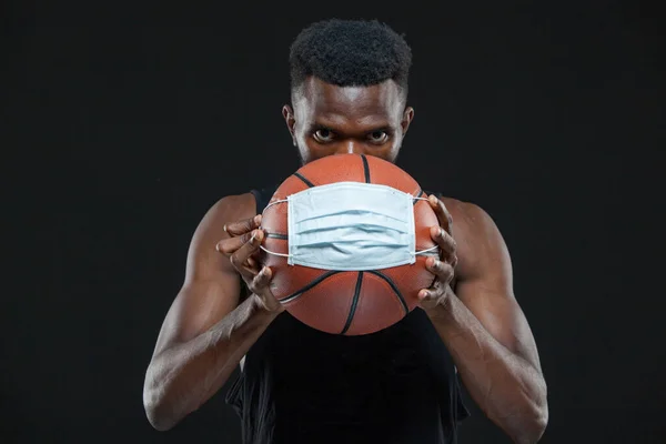 Siyah erkek basketbolcu koruyucu maskeli bir top tutuyor. Koronavirüs enfeksiyonu ve salgın hastalıkların yayılmasını önlüyor. Sağlık, tıp, spor konsepti — Stok fotoğraf
