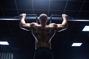 Manken görünümlü yakışıklı genç kaslı adam antrenman yapıyor spor salonunda sırt kaslarını şişiriyor ve makinelerle kilo alıyor.