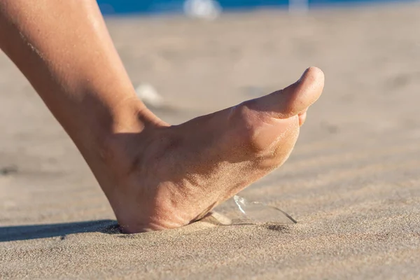 Frau geht an den Strand und riskiert, auf eine Scherbe aus Flaschenglas zu treten, die auf dem verdreckten Sand liegt — Stockfoto