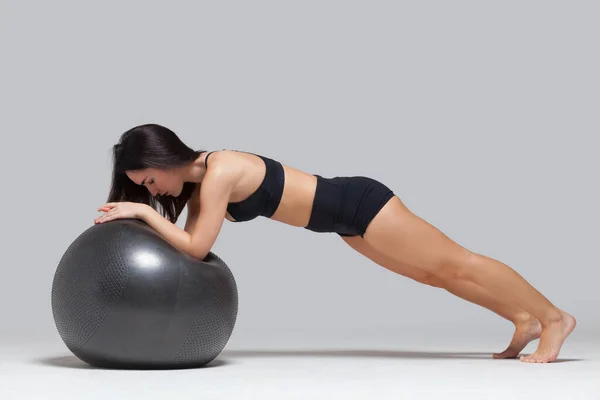 Tiro de comprimento total de jovem fitness menina morena fazendo exercícios com bola de fitness isolada no fundo cinza — Fotografia de Stock