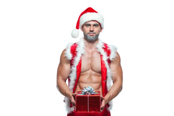 Sexy Santa Claus. Bodybuilder young handsome santa clause smile holds a gift in a red box and shows off abs cubes at New Years eve and Christmas winter holiday white background. — Stock Photo, Image