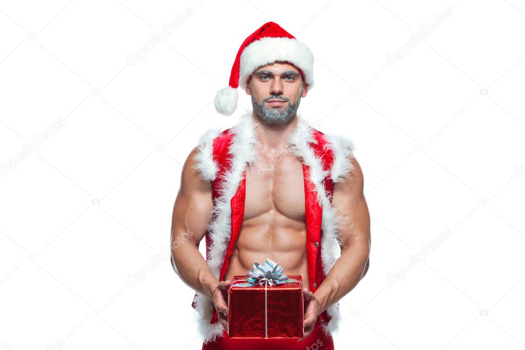 Sexy Santa Claus. Bodybuilder young handsome santa clause smile holds a gift in a red box and shows off abs cubes at New Years eve and Christmas winter holiday white background.