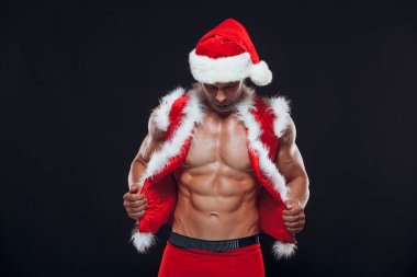 Seksi Noel Baba. Vücut geliştirici genç yakışıklı Noel Baba kılıklı gülümseme Noel Baba şapkası takıyor yeni yıl arifesinde karın kaslarını gösteriyor ve Noel tatilinin kara arka planında.
