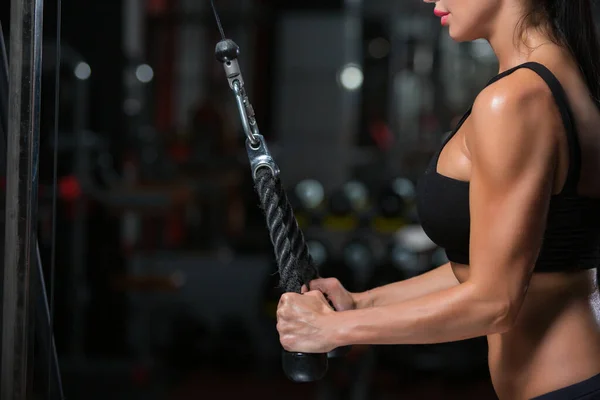 Close-up van sterke gespierde armen van jonge vrouw doen oefening op de triceps in de crossover in de sportschool — Stockfoto