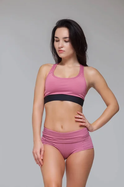 Atrakcyjna młoda brunetka w różowej odzieży sportowej pozuje na szarym tle — Zdjęcie stockowe