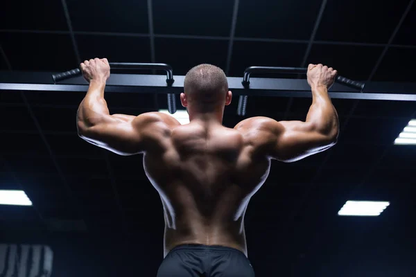 Pohledný mladý svalnatý muž vzhledu modelu cvičit čerpání zpět svaly v tělocvičně přibírá na váze na strojích — Stock fotografie