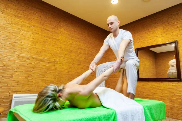 Vinkel vy skott på massör drar kvinna armar gör traditionell thailändsk massage på kvinnlig kropp i spa salongen. Begreppet skönhetsbehandling — Stockfoto