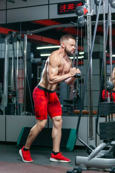 Starker muskulöser Mann trainiert seinen Trizeps mit Sportgeräten in der modernen Turnhalle — Stockfoto