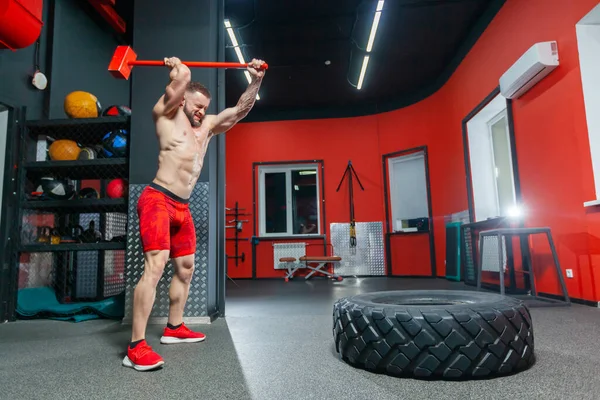 Ganzkörperporträt eines kräftigen, muskulösen Mannes, der im modernen Fitnessstudio mit dem Vorschlaghammer trainiert — Stockfoto