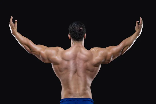 Achteraanzicht van een aantrekkelijke sporter die met opgeheven armen staat en zijn spieren op zwarte achtergrond laat zien — Stockfoto