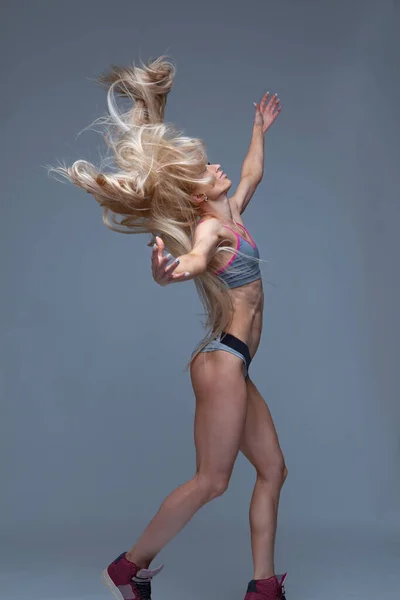Сексуальна спортивна блондинка кинула довге волосся ізольовано на сірому фоні — стокове фото
