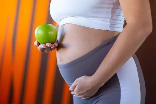 Close up of pregnant woman belly holding green apple, healthy pregnancy concept — Stock Photo, Image