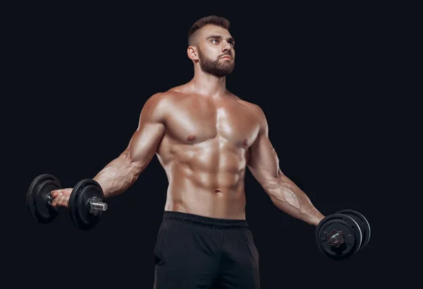 Sexy atlético hombre está mostrando cuerpo muscular con mancuernas de pie con la cabeza hacia abajo, aislado sobre fondo negro —  Fotos de Stock