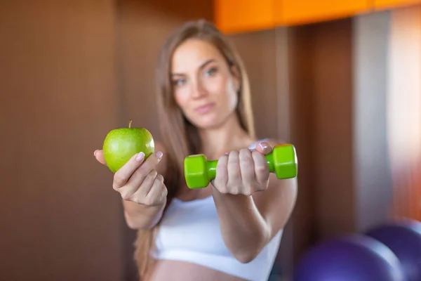 Zdjęcie uśmiechniętej ciężarnej kobiety wyciągającej ręce z zielonym jabłkiem i hantlem, zdrowa koncepcja ciąży — Zdjęcie stockowe