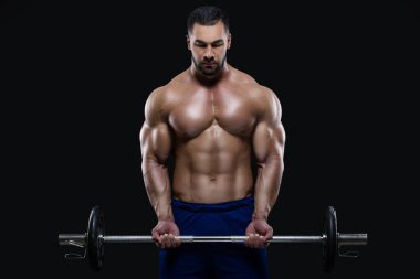 Yakışıklı fitness elemanı ağır bir halterle dikiliyor. Siyah arka planda çalışmaya hazır.