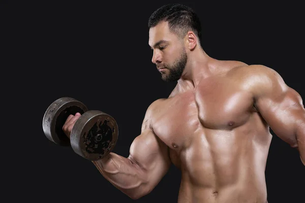 Un hombre guapo y musculoso se centra en realizar el ejercicio levantando una mancuerna con una mano aislada sobre fondo negro —  Fotos de Stock