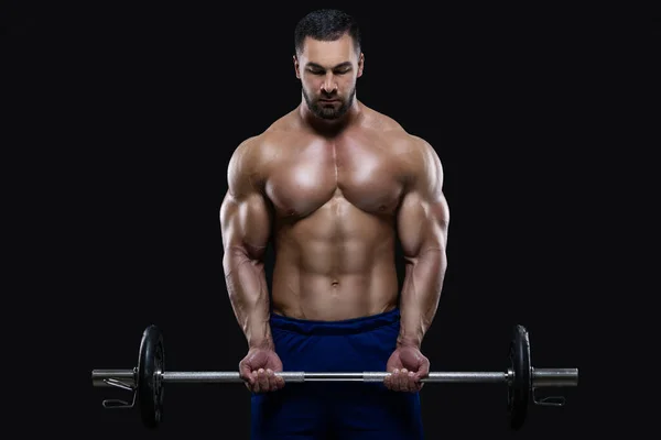 Guapo hombre de fitness está de pie con una pesada barra de pesas listo para entrenar aislado sobre fondo negro —  Fotos de Stock