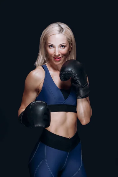 Cute blonde in boxing gloves smiles and prepares for training isolated on black background — Stock Photo, Image