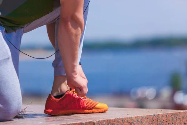 Close up on mans hands tying shoelaces on orange sneakers and a bottle of water during a run in a summer park — Stock Photo, Image