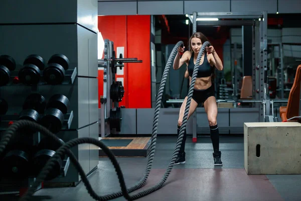 Full längd foto av attraktiv ung muskulös flicka med hjälp av träningsrep för rep motion i ett gym — Stockfoto