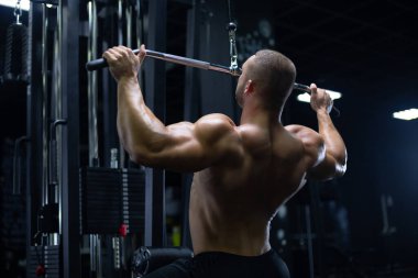 Manken görünümlü yakışıklı genç kaslı adam antrenman yapıyor spor salonunda sırt kaslarını şişiriyor ve makinelerle kilo alıyor.