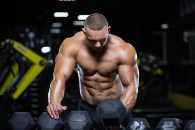 Genç yetişkin vücut geliştirici spor salonunda ağırlık kaldırmak için bir halter seçiyor.