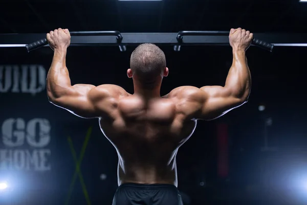 Manken görünümlü yakışıklı genç kaslı adam antrenman yapıyor spor salonunda sırt kaslarını şişiriyor ve makinelerle kilo alıyor. — Stok fotoğraf