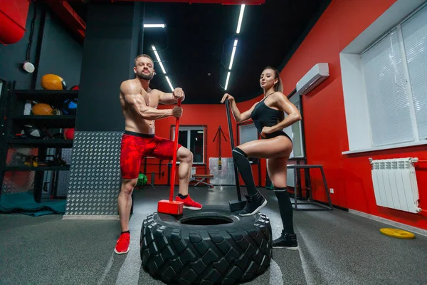 Портрет м'язистого сильного чоловіка і сексуальної фітнес-леді позує з їжаками і шиною в тренажерному залі — стокове фото