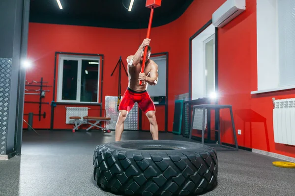 Pełna długość portret silnego muskularnego mężczyzny wykonującego trening młotem kowalskim w nowoczesnej siłowni — Zdjęcie stockowe