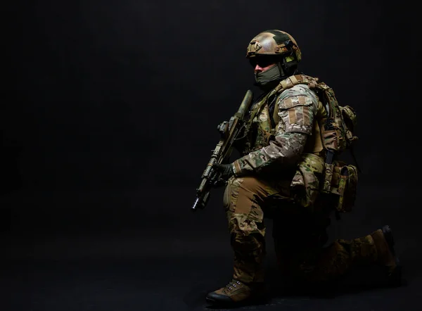 Полноразмерный портрет армейского солдата в полном военном снаряжении, шлеме, очках и маске, стоящего на одном колене в ожидании команды, изолированного на черном фоне — стоковое фото