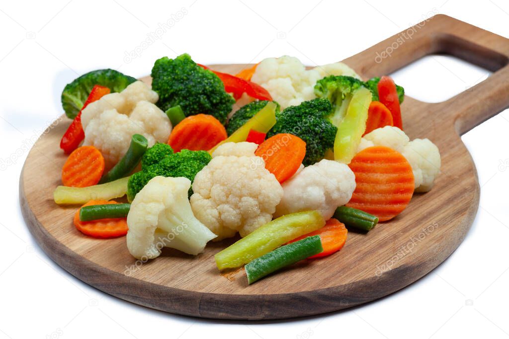 Top view of frozen mixed vegetables cauliflower, carrots, broccoli, sliced bell peppers lying on wooden cutting board