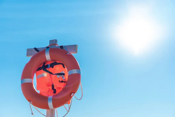 Bright lifebuoy and life jacket on the beach against the blue sky
