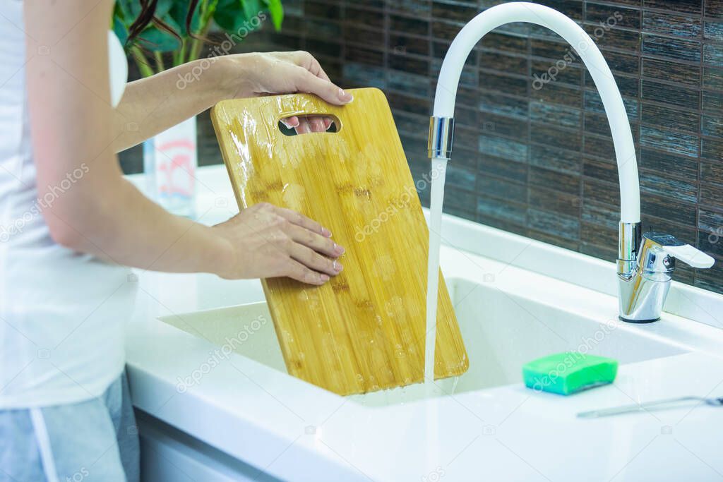 Close up shot of girl washing a wooden cutting board in the modern kitchen in the white sink