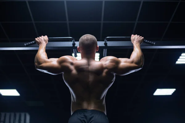 Manken görünümlü yakışıklı genç kaslı adam antrenman yapıyor spor salonunda sırt kaslarını şişiriyor ve makinelerle kilo alıyor. — Stok fotoğraf