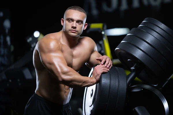 Manken görünümlü genç kaslı atlet spor salonunda disklerin yanında duran kasları çalıştırdıktan sonra dinleniyor. — Stok fotoğraf