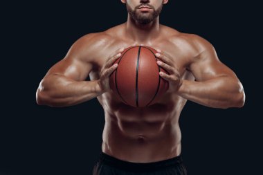 Close up of a basketball held by a muscular player with naked torso ready to throw, isolated on black background