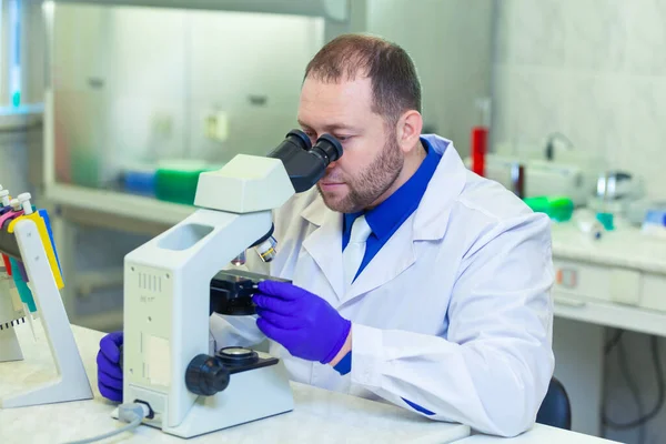 Especialista mirando a través del microscopio realizando investigación científica en un laboratorio. Prueba de orina. COVID-19. COVID Coronavirus —  Fotos de Stock