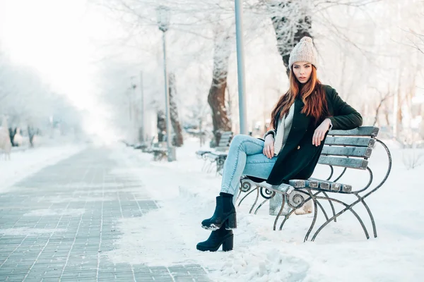 Mladá žena ve winter parku sedí na lavičce — Stock fotografie