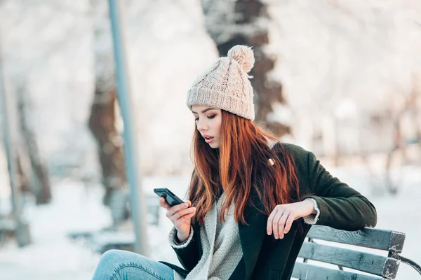Νεαρή γυναίκα στο χειμερινό πάρκο μιλάμε κινητό τηλέφωνο, sms, κάθονται στον πάγκο — Φωτογραφία Αρχείου