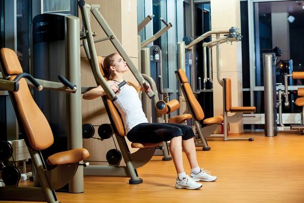 Esporte, fitness, estilo de vida e conceito de pessoas - jovem mulher flexionando músculos na máquina de ginásio — Fotografia de Stock