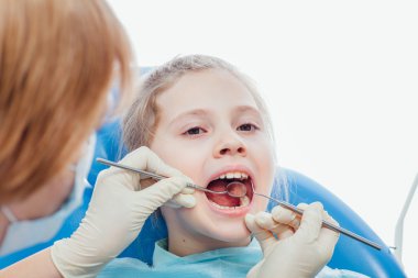 Küçük kız dişçi ofisinde oturuyor.