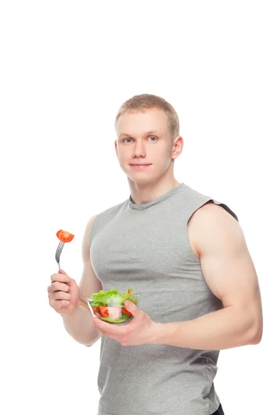 Junger glücklicher muskulöser Mann isst einen Salat vor weißem Hintergrund. — Stockfoto