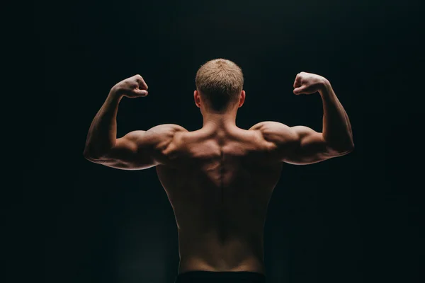 Muskularny mężczyzna młody pokazano jego biceps na białym tle na czarnym tle. — Zdjęcie stockowe