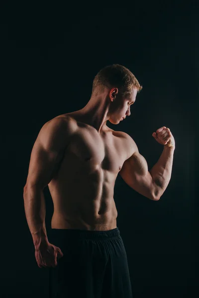 Jovem muscular mostrando seu bíceps isolado no fundo preto . — Fotografia de Stock