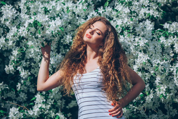 Beautiful young woman with gorgeous curly fair outdoors,flowering
