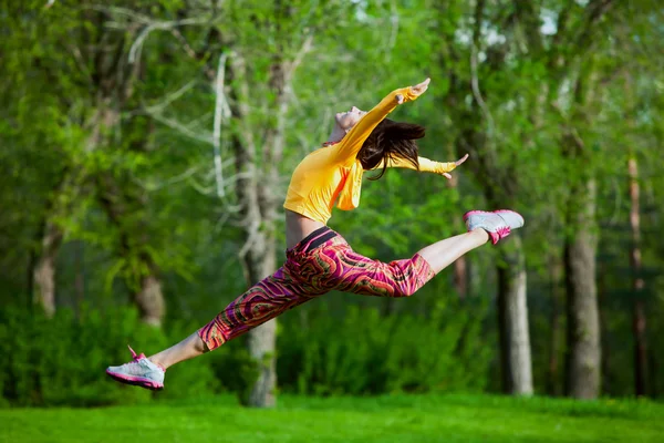 Ung vacker flicka gör gymnastiska hopp utomhus — Stockfoto