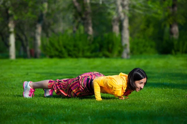 Press ups exercise by young woman. Girl working out on grass crossfit strength training in the glow of morning sun — Stock Photo, Image