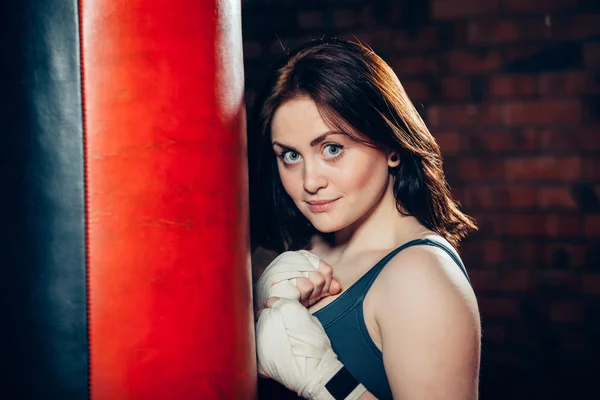 Young woman boxing  posing near a punching bag in bandages — Stock Photo, Image