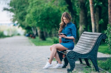 Bankta tablet bilgisayar kullanan bir genç kadın yan görünüm