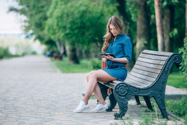 Seitenansicht einer jungen Frau mit Tablet-Computer auf Parkbank — Stockfoto